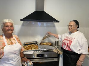 Two of CHL's residents dressed in aprons in front of a new large oven with trays of fresh baked items.