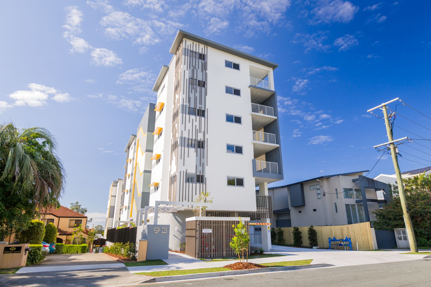 A white, six story apartment building. It has landscaping at the bottom, large windows and balconies visible.