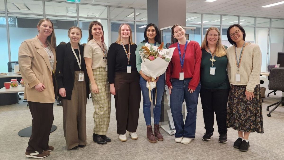 A picture of Priya from the homelessness services team. She is holding flowers and members of her team are in the picture with her.