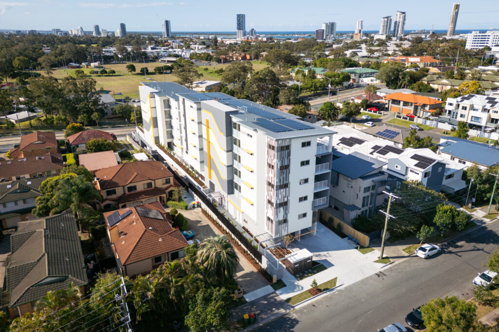 An arial view of a regional city featuring a range of home type with a multi story apartment building as the main focus of the photo.