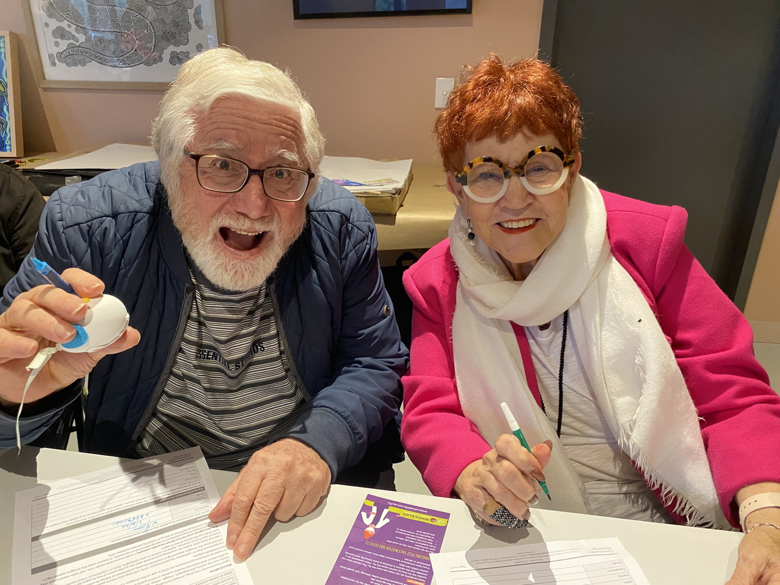 Two older people sitting and smiling at the camera, one is holding an Easter Egg.