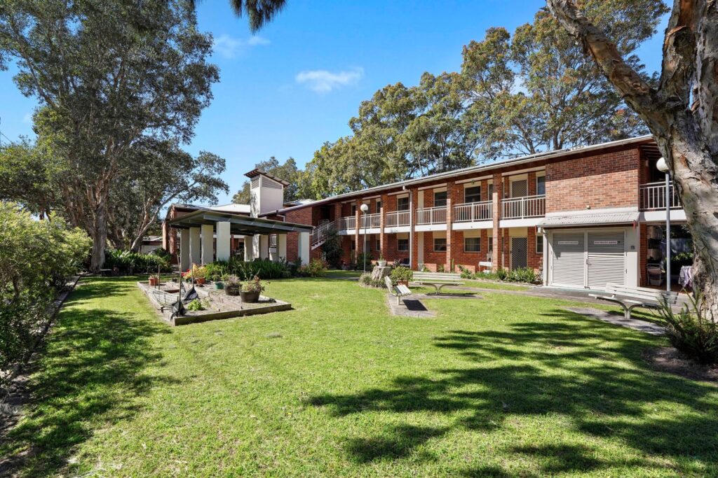 An image of a two story L shaped brick development of units with a garden in the front.