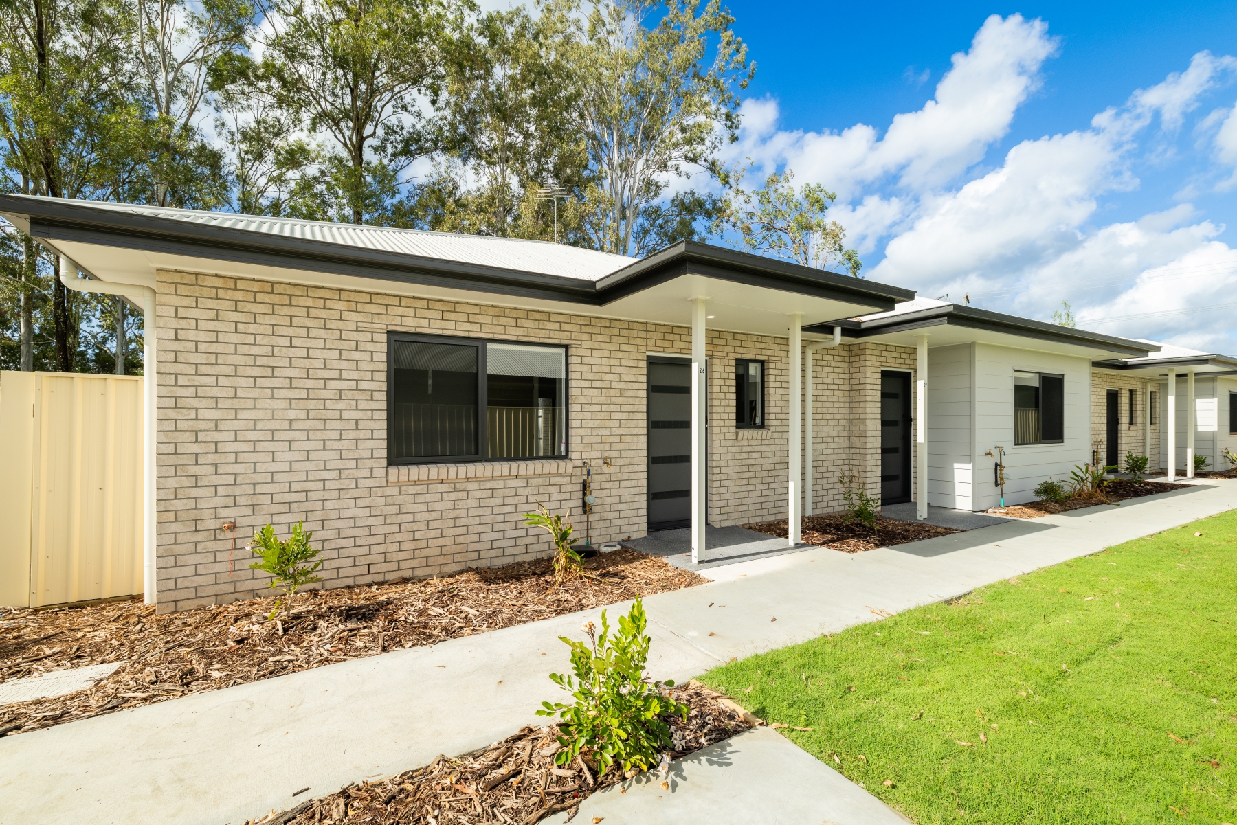 Image of small detached unit in a small block. White walls and dark roof. Grass and shrubs out the front.